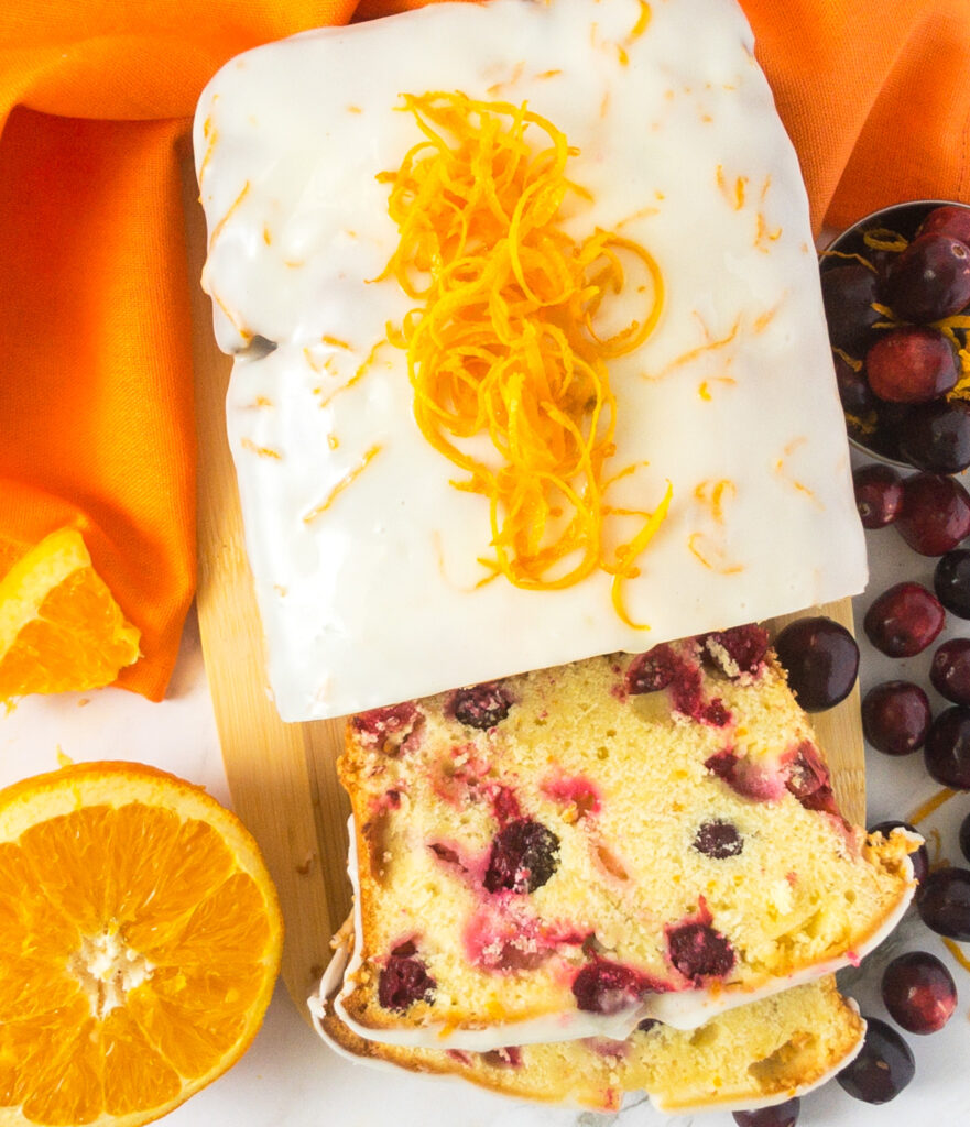 Orange Cranberry loaf cake cir rounded by oranges and cranberries