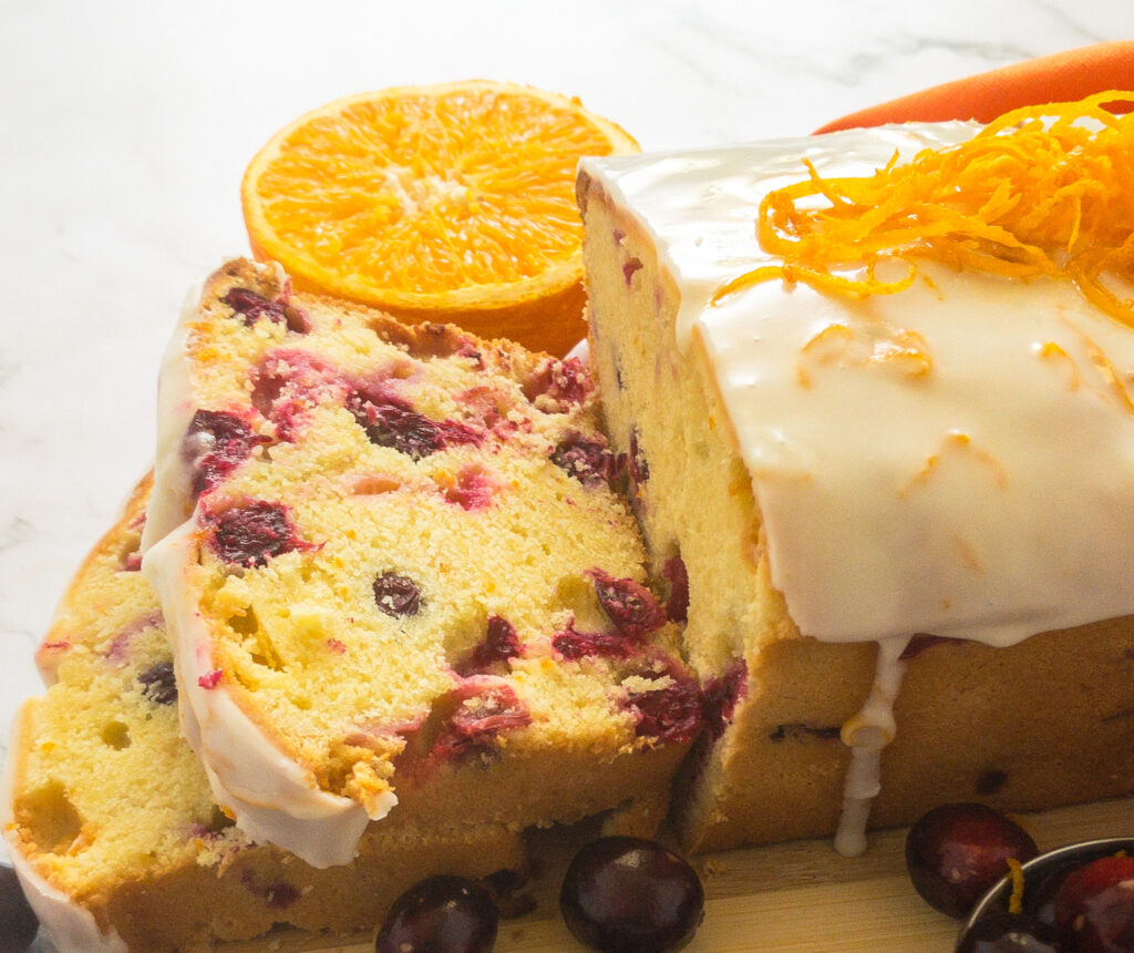 Orange Cranberry loaf cake cir rounded by oranges and cranberries